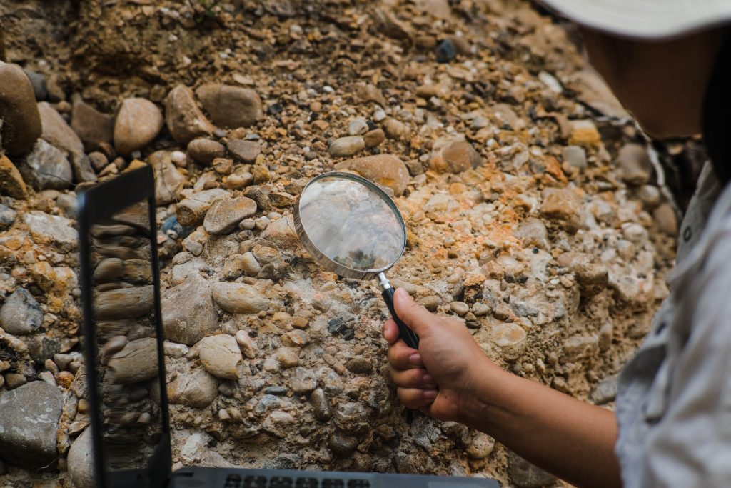 Close-up of female geologist using magnifying glass to examine and analyze rock, soil, sand in nature. Archaeologists explore the field. Environmental and ecology research.