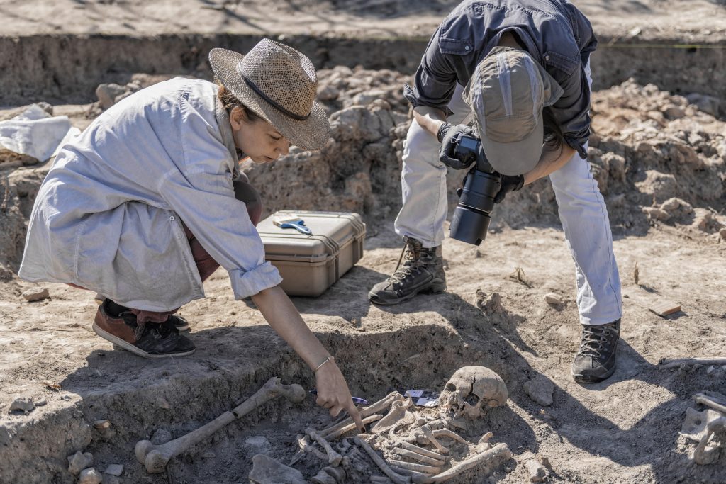 Young archaeology researchers documenting ancient burial site with camera.